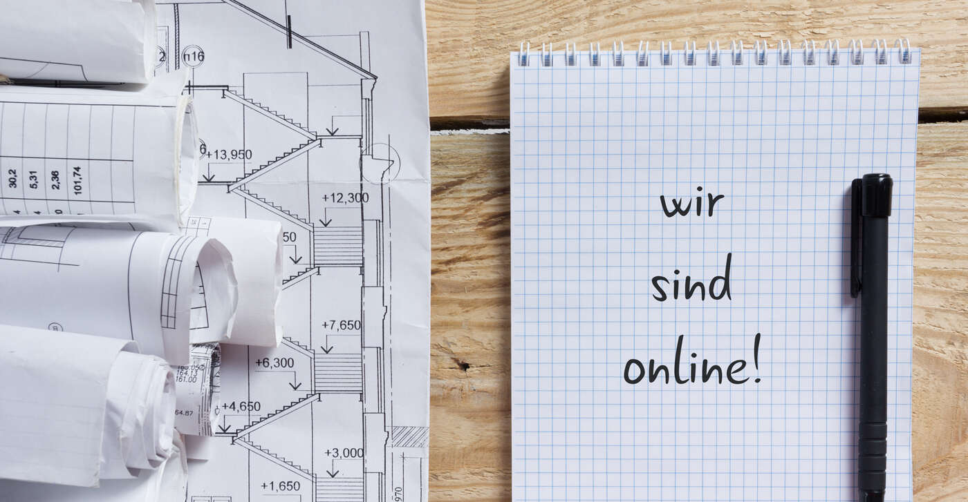 Auf einem Holztisch liegen Pläne und ein Zettel mit Stift, wo oben steht: Wir sind online!